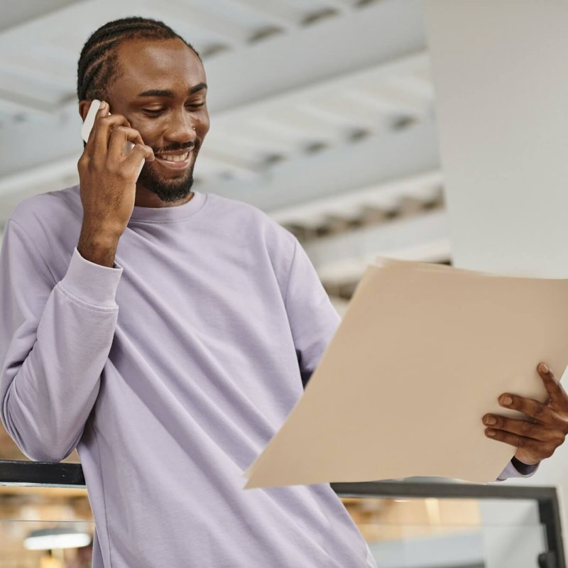 happy-african-american-man-looking-at-project-on-paper-talking-on-smartphone-planning-startup