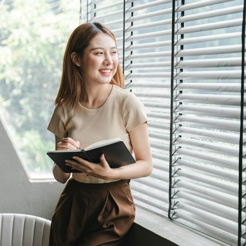 smiling-asian-woman-holding-a-note-in-hand-and-standing-near-window-startup-business-asian-woman-onl